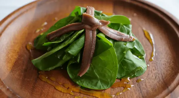 Cogollos frescos con anchoas cruzadas, aderezados con aceite dorado sobre plato de madera.