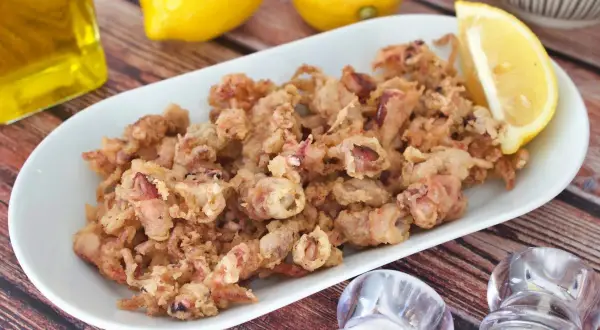 Crujientes puntillas de calamar fritas en un plato blanco, acompañadas de limón y aceite de oliva.