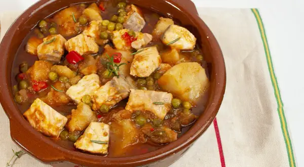 Un delicioso marmitako de salmón, con trozos de pescado, patatas, guisantes y pimientos rojos en una cazuela de barro.
