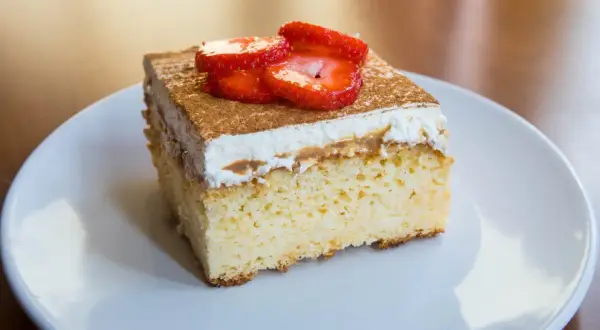 Un trozo de tarta 3 leches, esponjoso y cubierto con crema batida, canela y fresas frescas.