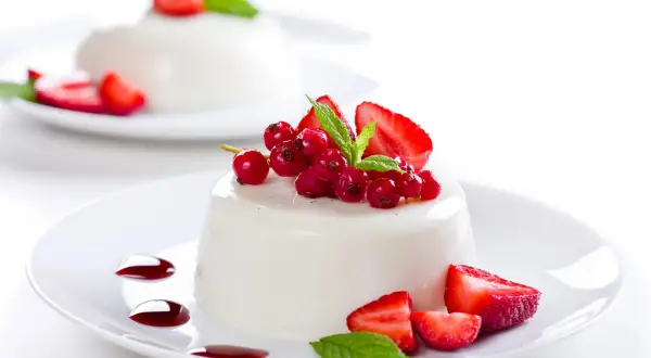 Deliciosa panna cotta receta, decorada con fresas, grosellas rojas y menta.