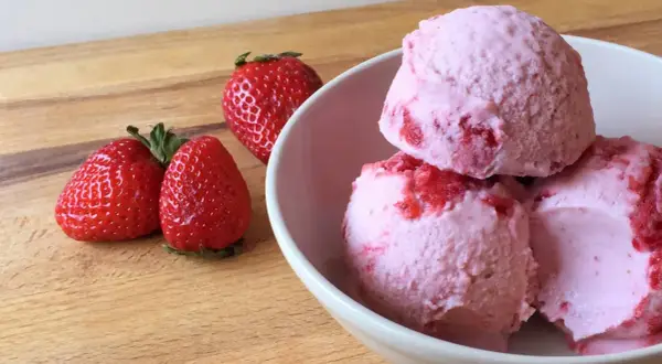 Bol con helado de fresa cremoso y trozos de fruta fresca.