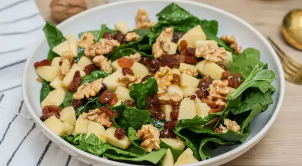 Deliciosa ensalada de espinacas con trozos de manzana, pasas y nueces. Una combinación crujiente y dulce.