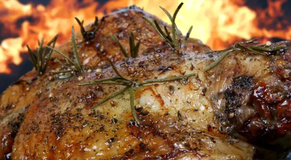 Pierna de cordero al horno, dorada y jugosa, con romero y especias, sobre un fondo de llamas. ¡Un festín irresistible!