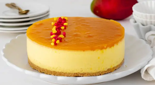 Deliciosa tarta de mango con una capa superior de gelatina brillante y decorada con granos rojos y amarillos.