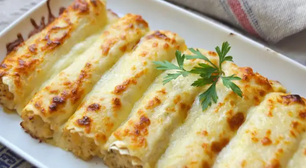 Canelones de pollo gratinados, cubiertos con queso derretido y dorados, decorados con perejil fresco.