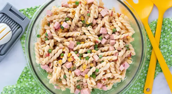 Ensalada de pasta con jamón, guisantes y maíz, lista para servir con su salsa para ensalada de pasta.
