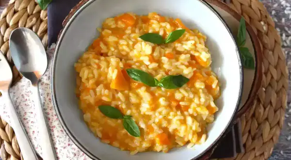 Cremoso risotto de calabaza, adornado con hojas de albahaca fresca, servido en un cuenco rústico.