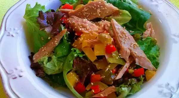 Ensalada de ventresca con pimientos de colores y semillas de sésamo, servida sobre hojas verdes frescas.