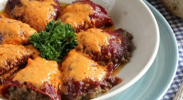 Pimientos rellenos de carne cubiertos con una cremosa salsa, decorados con perejil fresco.