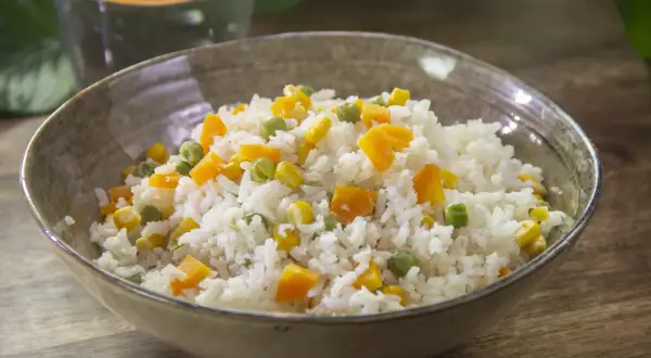 Un plato de arroz blanco con guisantes, maíz y zanahoria en cubitos. Una receta de arroz con verduras sencillo y colorido.