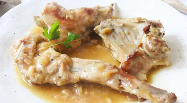 Sabroso conejo en salsa, servido en un plato blanco con una ramita de perejil.