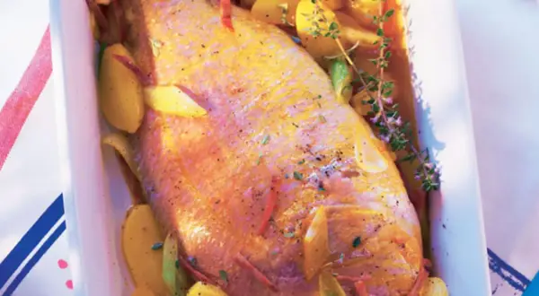 Pescado rosado al horno con patatas y hierbas aromáticas en una bandeja blanca.