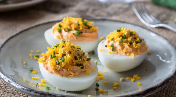 Huevos rellenos de atún, decorados con ralladura de huevo y cebollino. Un aperitivo delicioso y fácil de preparar.