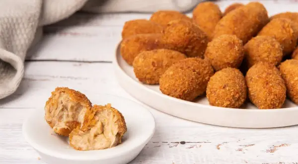Croquetas de puchero doradas y crujientes, una de ellas partida mostrando su interior cremoso.