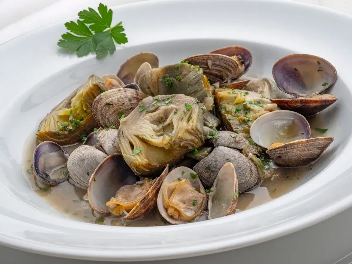 Delicioso plato de alcachofas con almejas, un manjar marino y vegetal en una salsa suave.