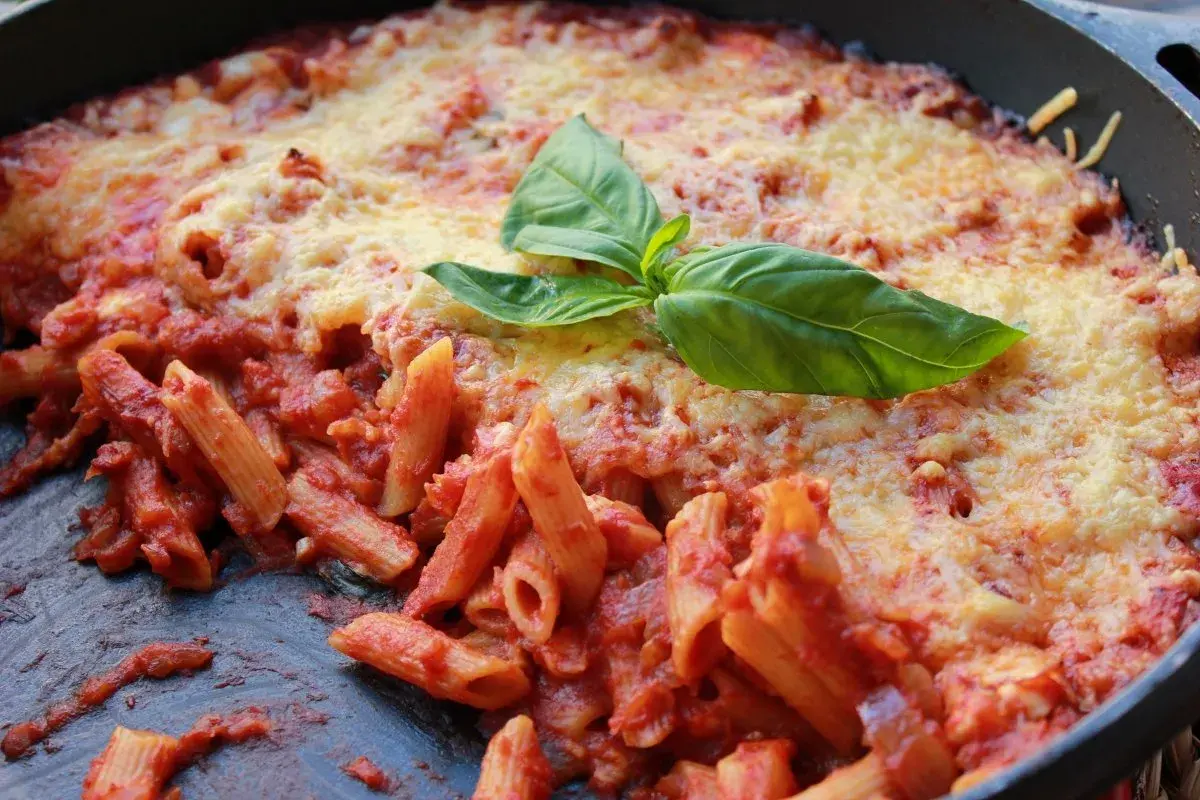 Macarrones al horno con salsa de tomate y queso gratinado, decorados con hojas de albahaca fresca. ¡Un plato casero irresistible!