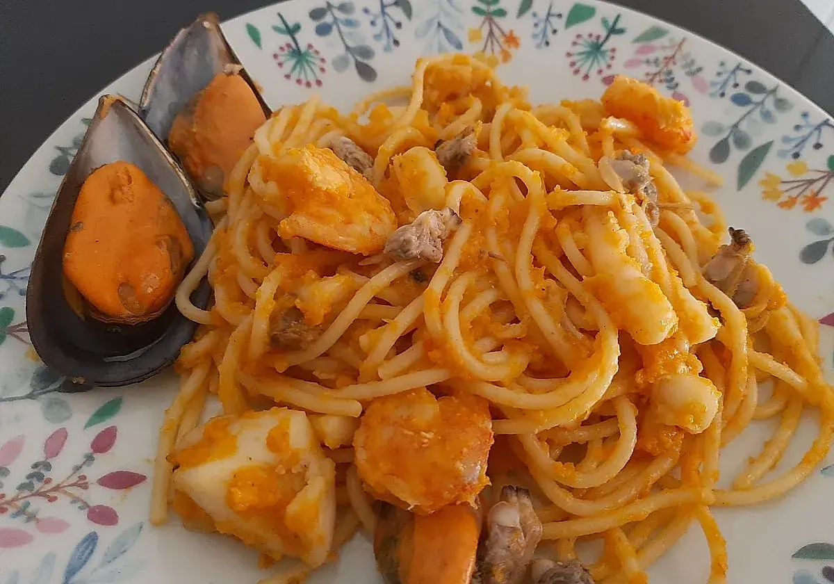 Espaguetis a la marinera con mejillones, gambas y calamares, servidos en un plato con un delicado estampado floral.