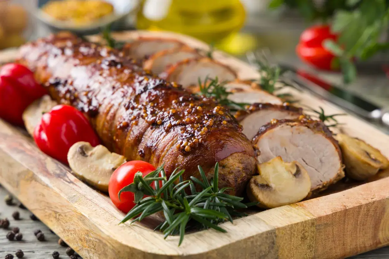 Lomo de cerdo al horno jugoso, glaseado y especiado, servido con champiñones, pimientos rojos y romero en tabla de madera.