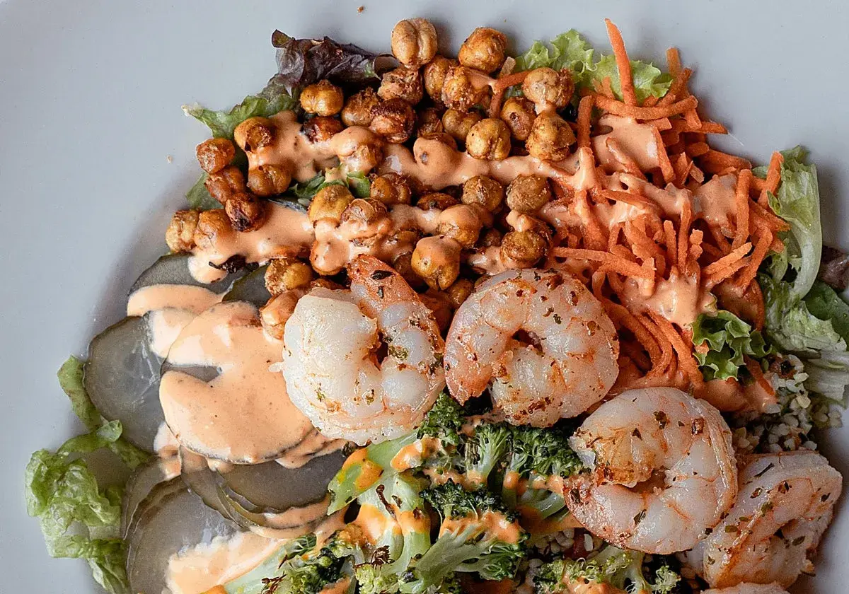 Ensalada fresca con garbanzos crujientes, langostinos jugosos, brócoli, zanahoria rallada y pepinillos encurtidos, todo bañado en una cremosa salsa rosada.