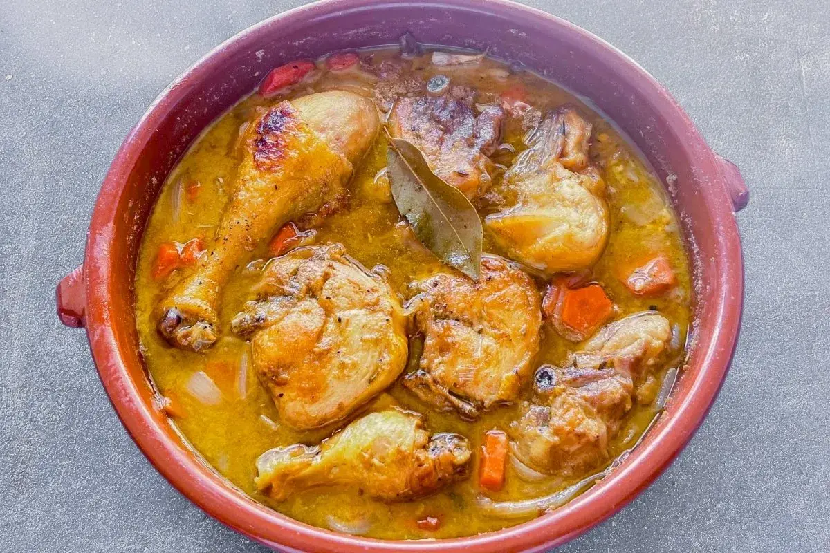 Muslos de pollo en salsa, un plato casero que evoca la receta de la abuela, con trozos de zanahoria y laurel.