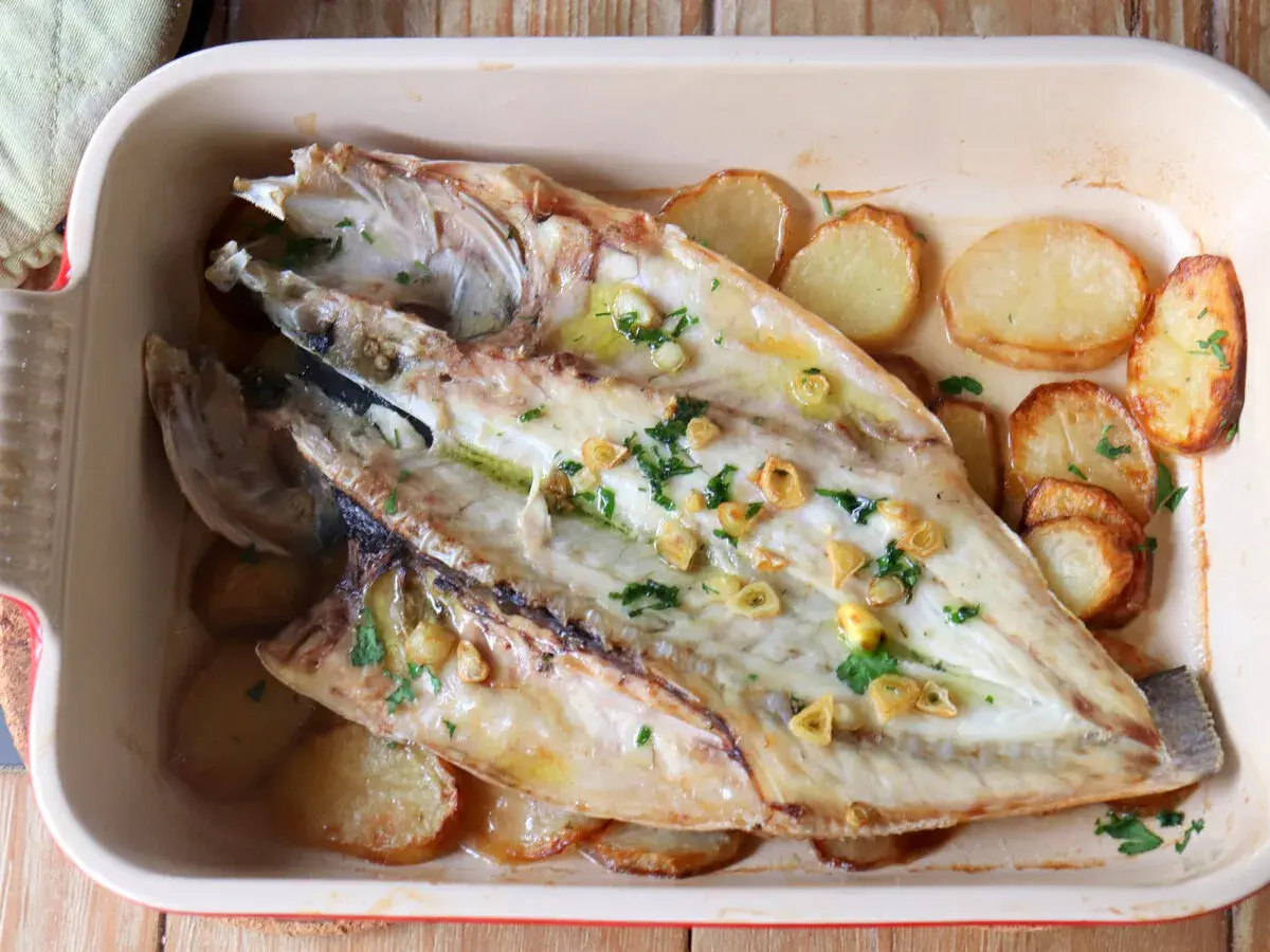 Lubina a la espalda horneada con patatas, ajo y perejil en una bandeja.
