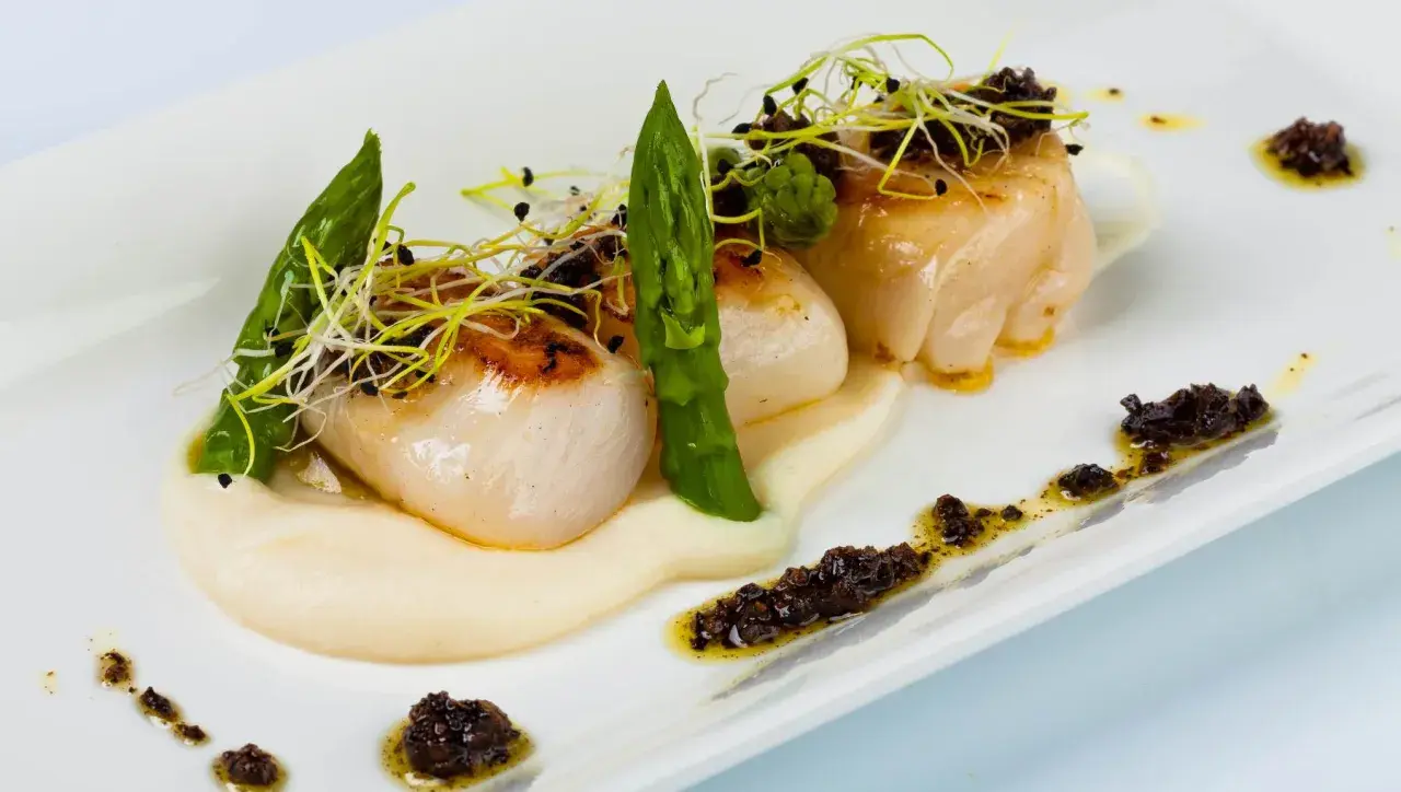 Deliciosas vieiras a la plancha sobre puré cremoso, adornadas con espárragos tiernos y brotes frescos. Un plato elegante y sabroso.