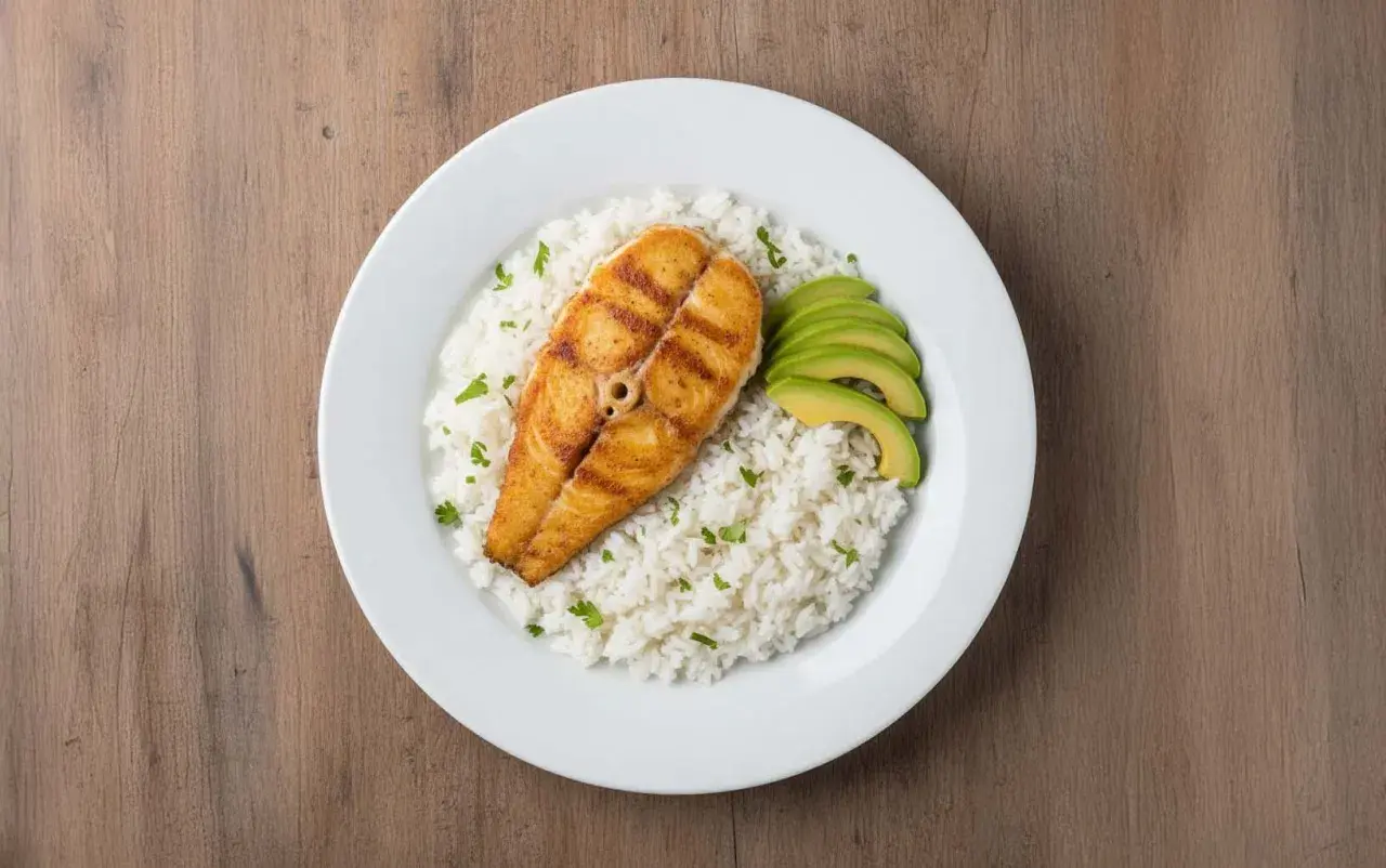 Un delicioso plato de arroz con pescado a la parrilla, acompañado de aguacate en rodajas y perejil picado.