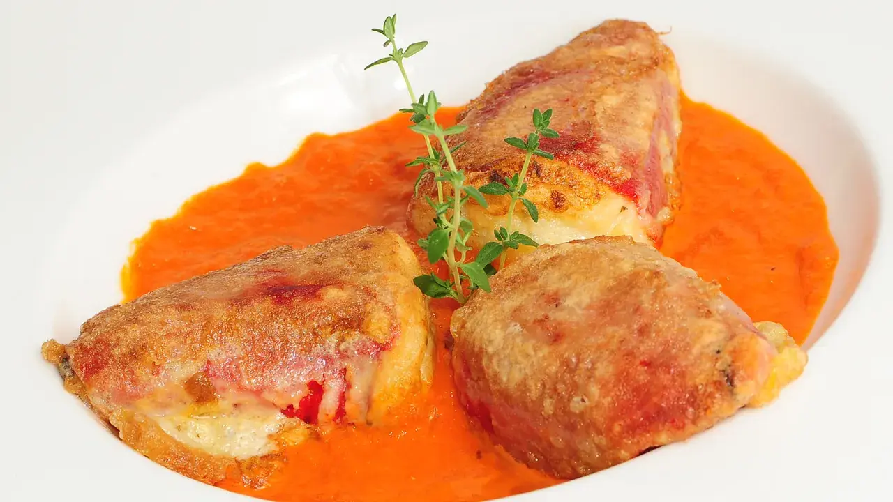 Pimientos rellenos de bacalao, dorados y crujientes, servidos en una cremosa salsa de pimientos rojos, adornados con tomillo fresco.