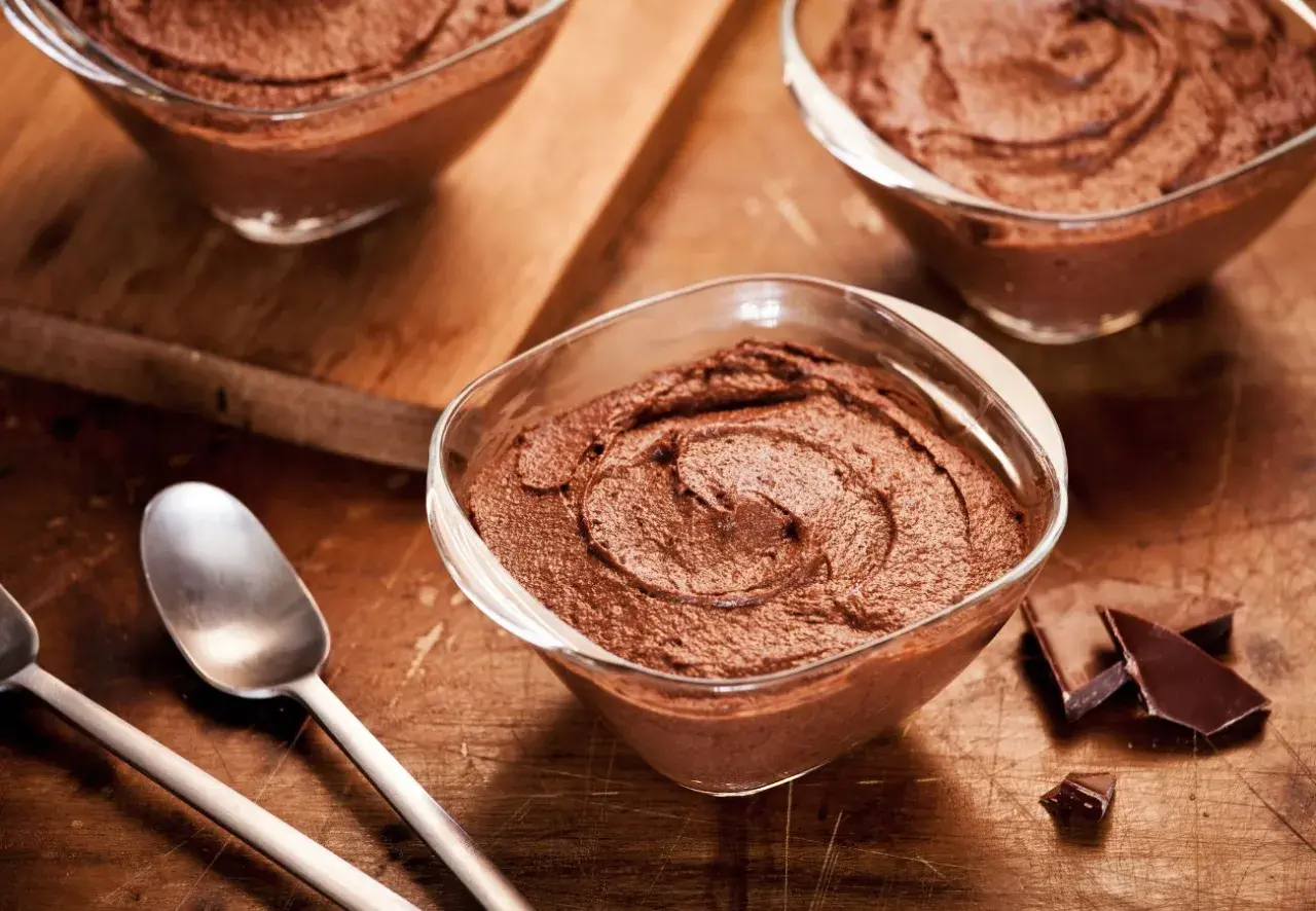 Delicioso mousse de chocolate en copas de cristal, listo para disfrutar. Trozos de chocolate negro al lado.