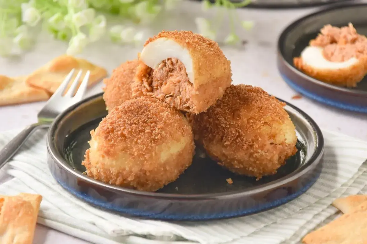 Deliciosos huevos rellenos rebozados, crujientes por fuera y jugosos por dentro, servidos en un plato con galletas saladas.