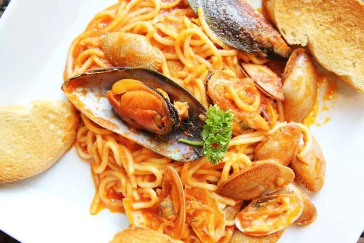 Espaguetis con almejas y mejillones en salsa roja, servidos con pan tostado. Un plato de pasta marinera delicioso.