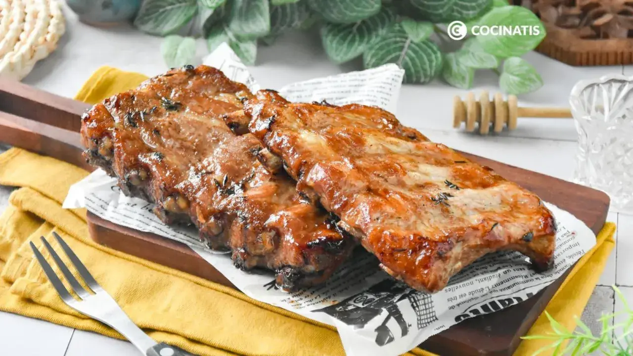 Costillas a la miel, jugosas y glaseadas, servidas sobre papel de periódico y tabla de madera.