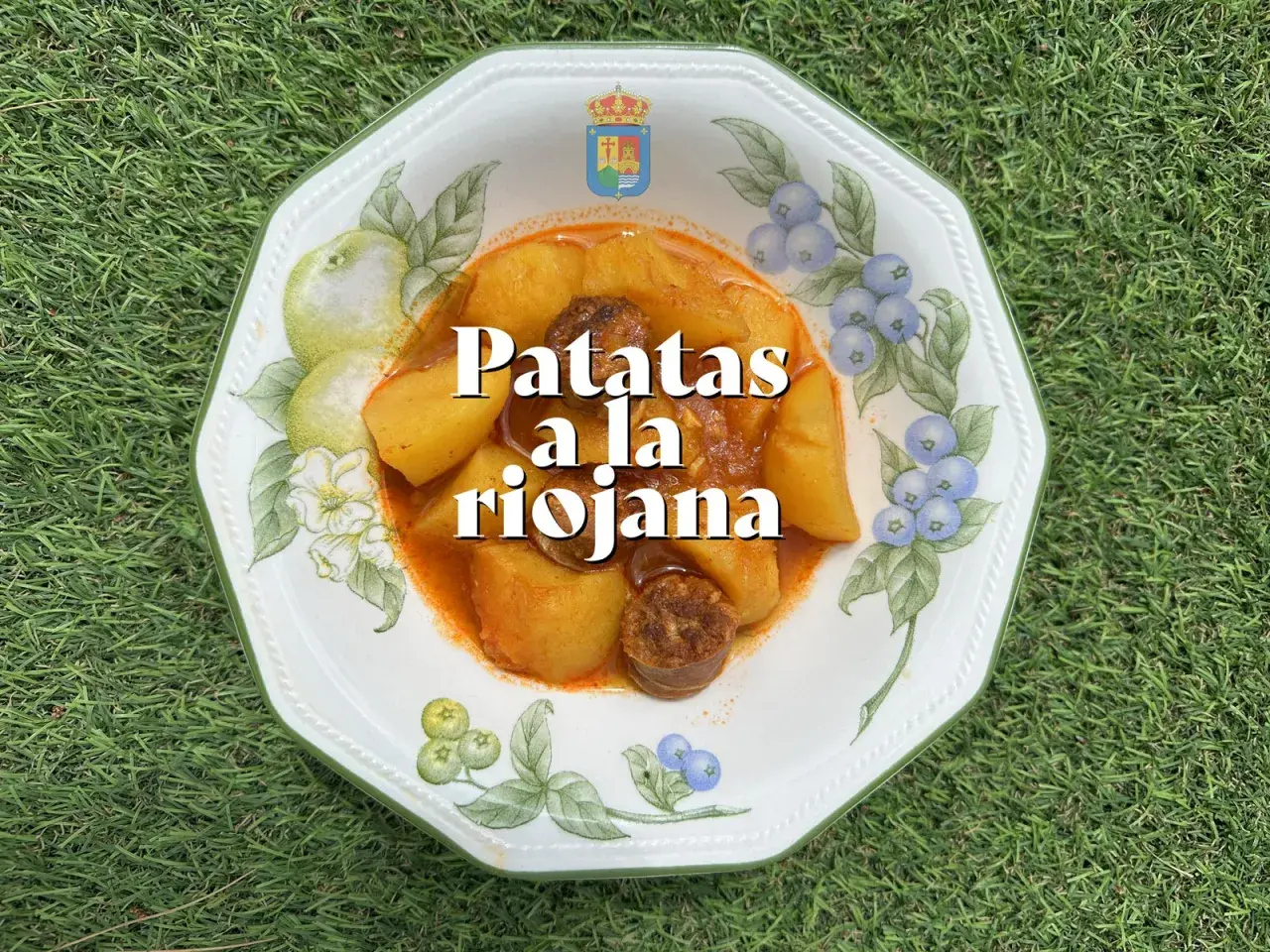Un plato de patatas a la riojana, con trozos de chorizo y patata en una salsa rojiza, servido en una vajilla decorada con frutas y bayas.