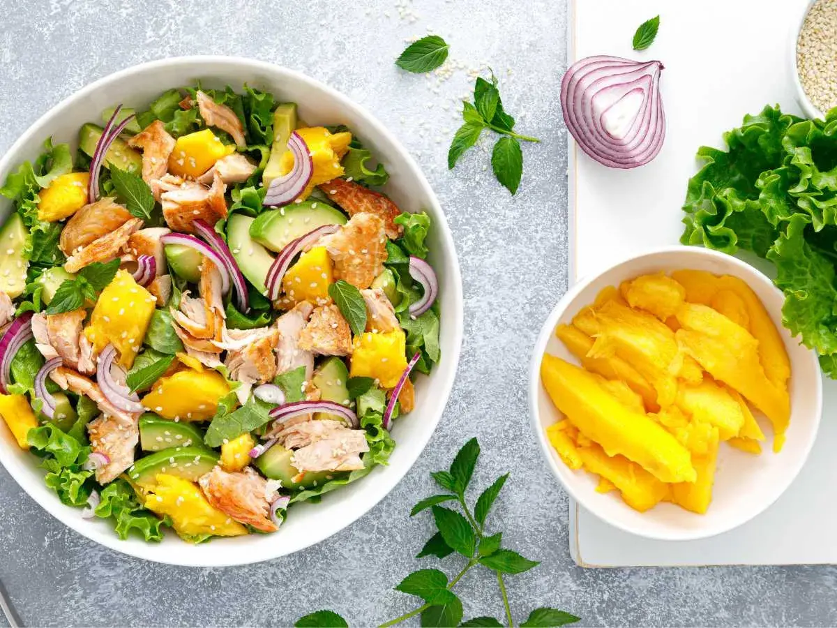 Ensalada de mango con salmón desmenuzado, aguacate, cebolla morada y hojas verdes. ¡Una explosión de sabor!