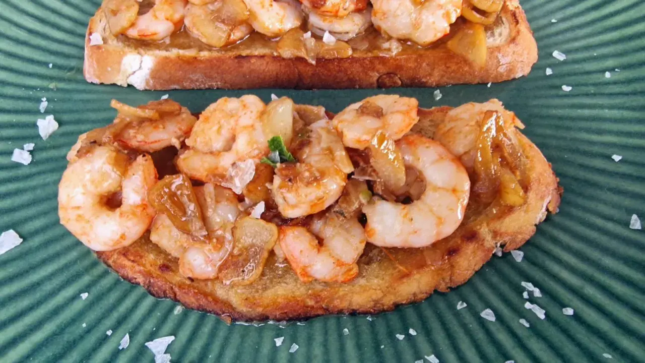 Tostadas con gambones al ajillo, cubiertas de ajo y perejil, espolvoreadas con sal marina gruesa sobre un plato verde.