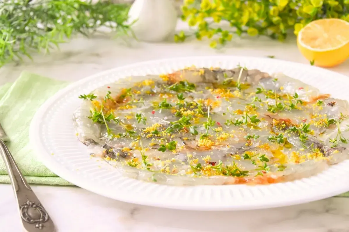 Delicado carpaccio de gambas con hierbas frescas y ralladura de limón, listo para disfrutar.