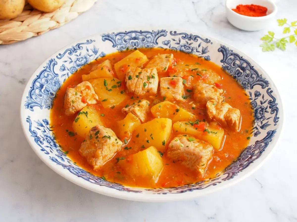 Un delicioso marmitako de atún con patatas y pimientos rojos, servido en un plato con borde azul y blanco.