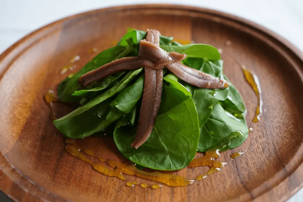 Cogollos frescos con anchoas cruzadas, aderezados con aceite dorado sobre plato de madera.