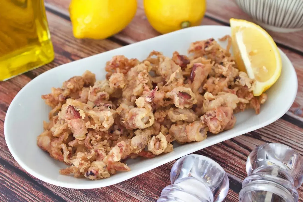 Crujientes puntillas de calamar fritas en un plato blanco, acompañadas de limón y aceite de oliva.