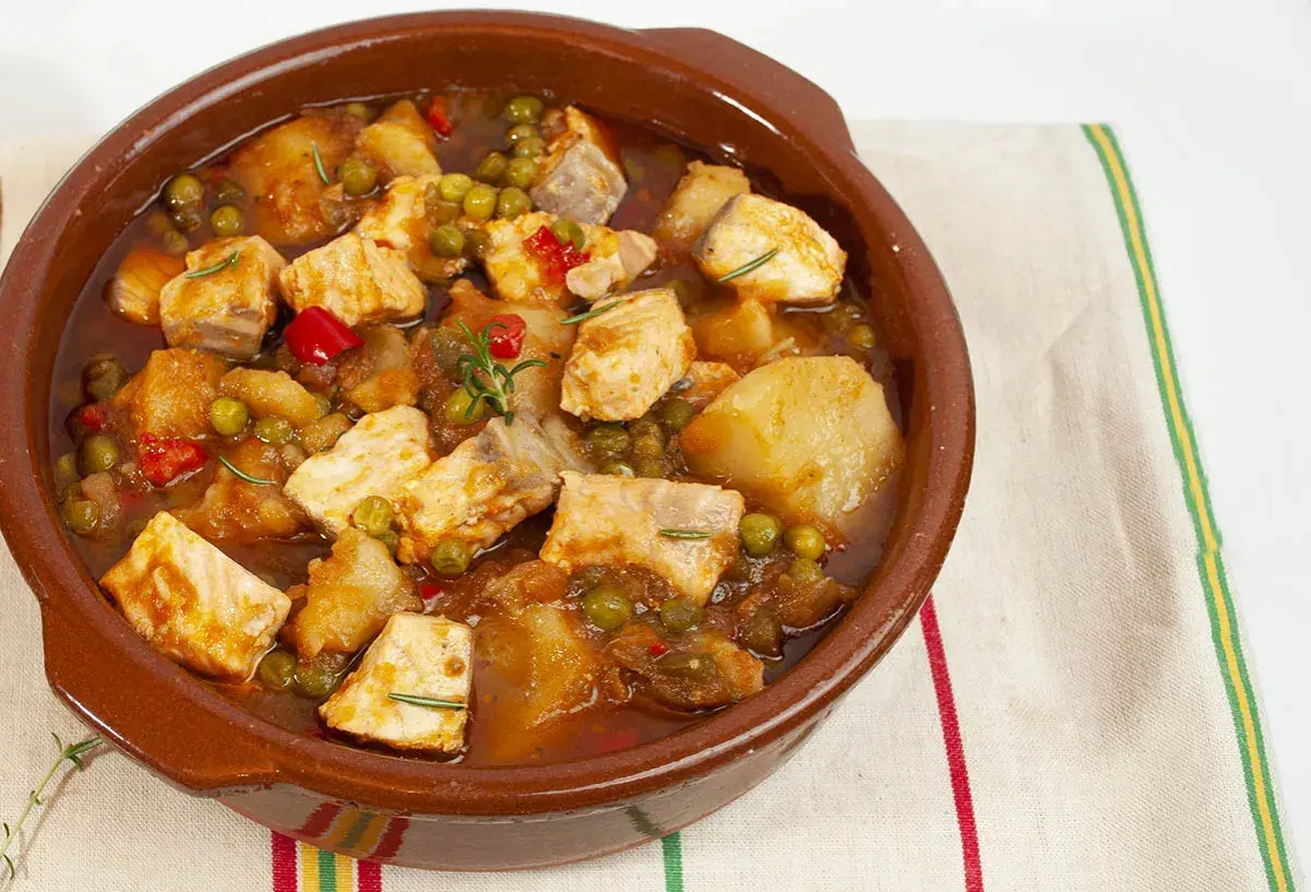 Un delicioso marmitako de salmón, con trozos de pescado, patatas, guisantes y pimientos rojos en una cazuela de barro.