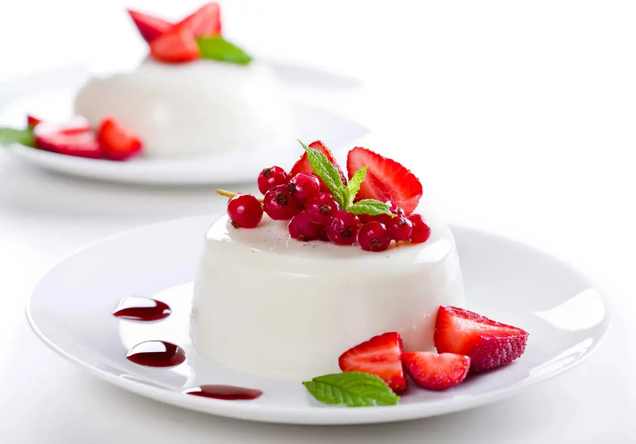 Deliciosa panna cotta receta, decorada con fresas, grosellas rojas y menta.