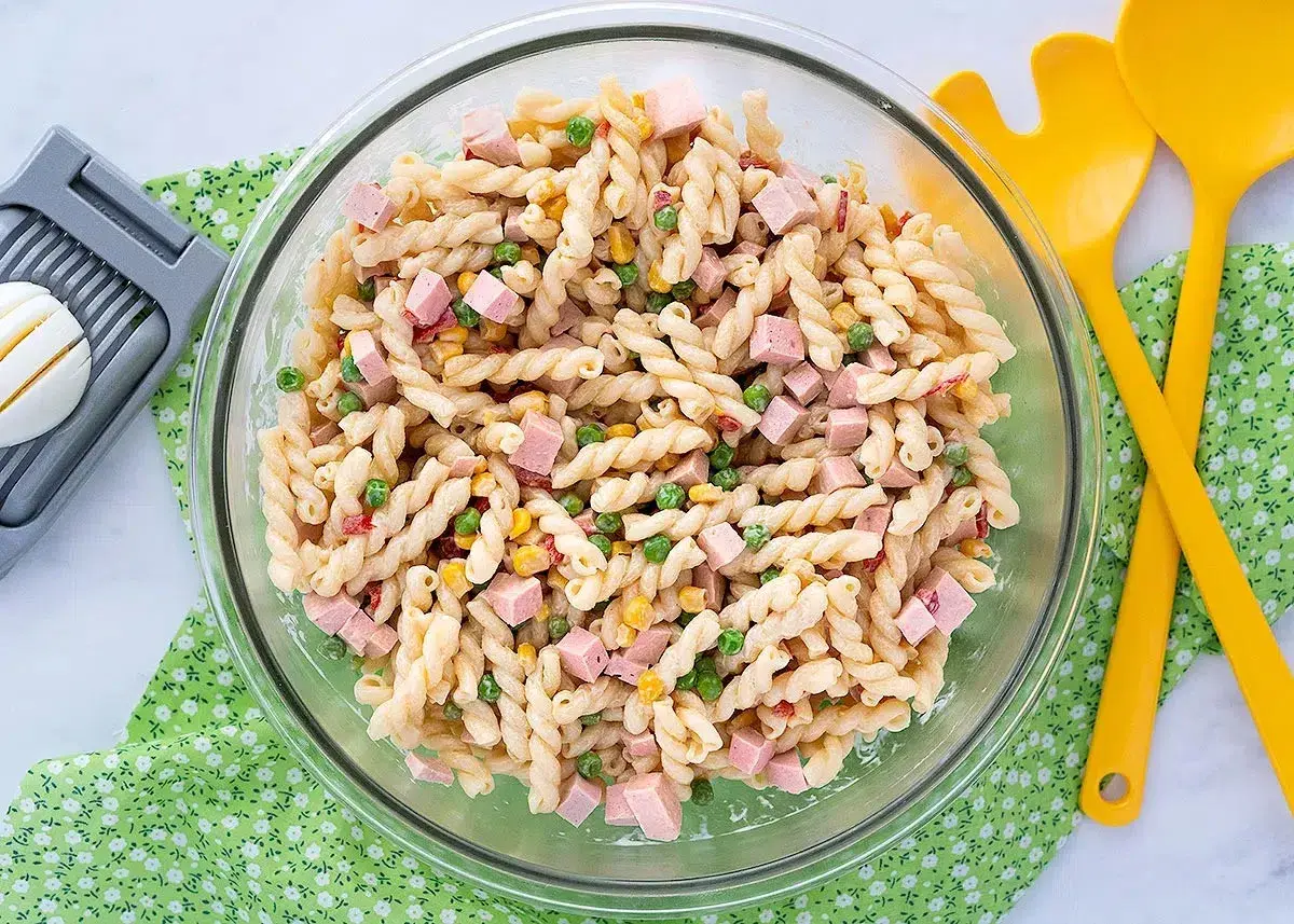 Ensalada de pasta con jamón, guisantes y maíz, lista para servir con su salsa para ensalada de pasta.