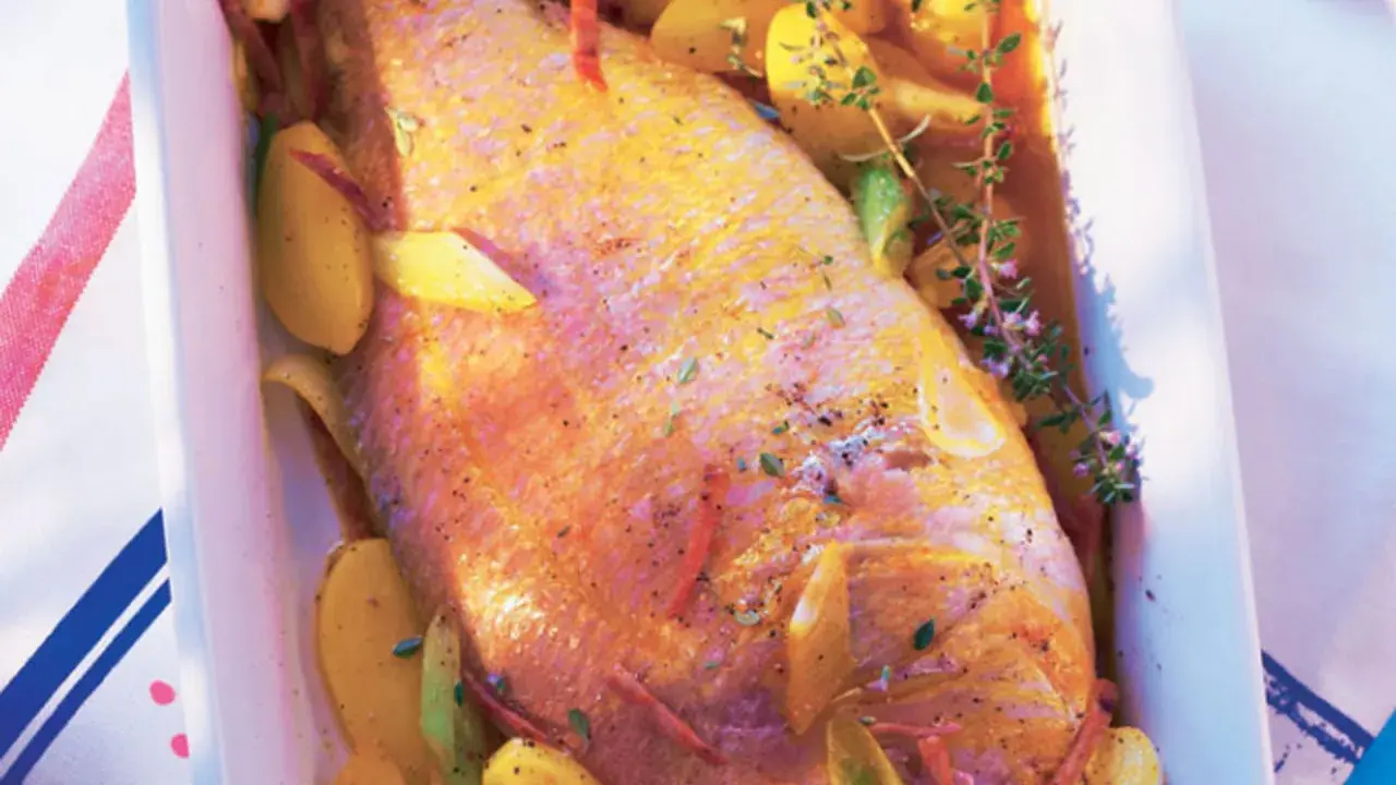 Pescado rosado al horno con patatas y hierbas aromáticas en una bandeja blanca.