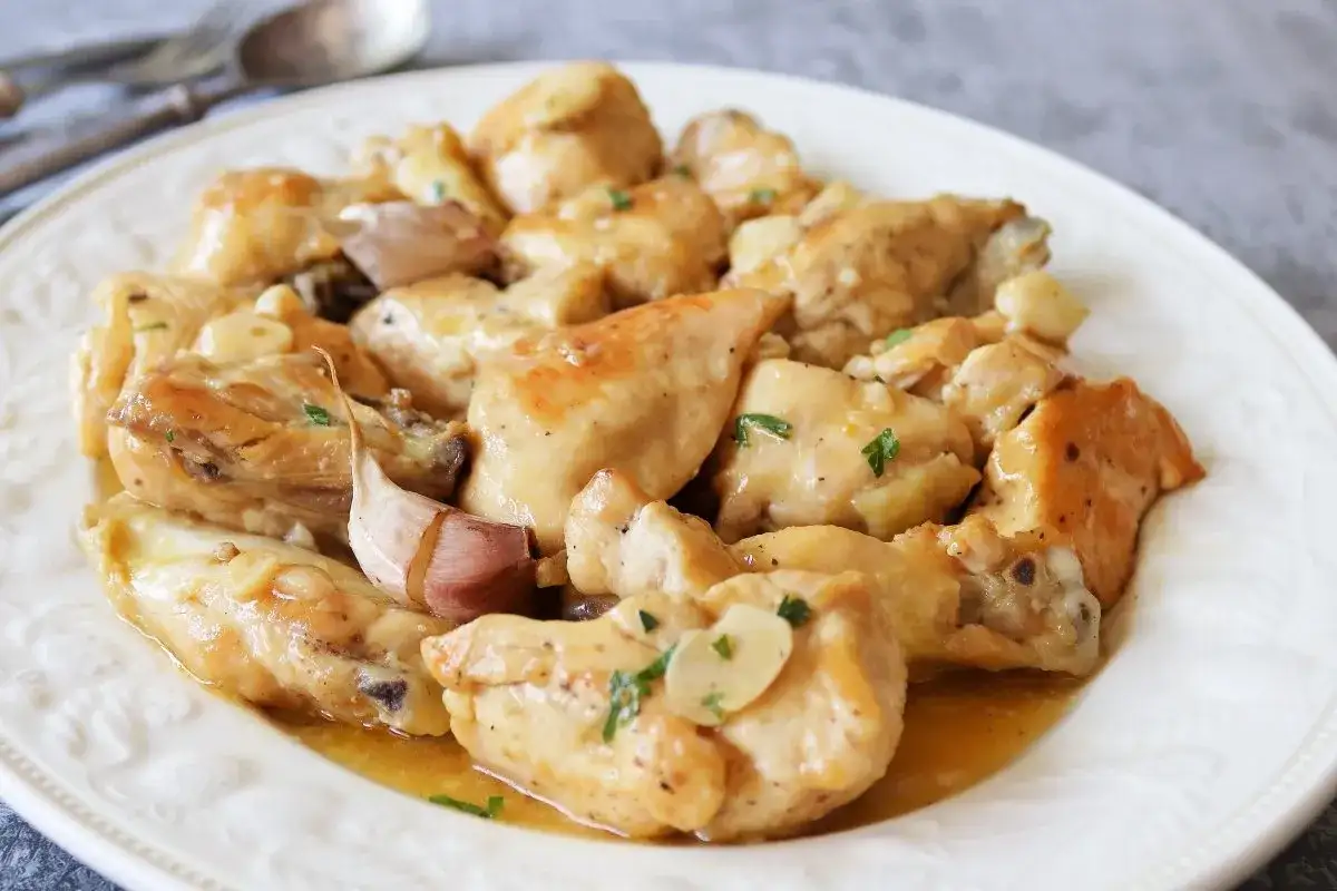 Sabroso pollo al ajillo servido en un plato blanco, con trozos de pollo dorados y dientes de ajo enteros.