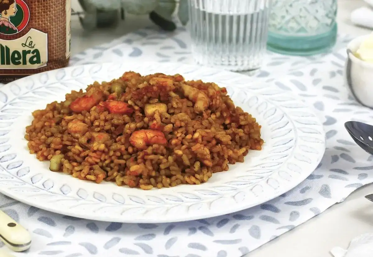 Delicioso arroz a banda con gambas y trozos de pescado, servido en un plato blanco con un borde decorado.