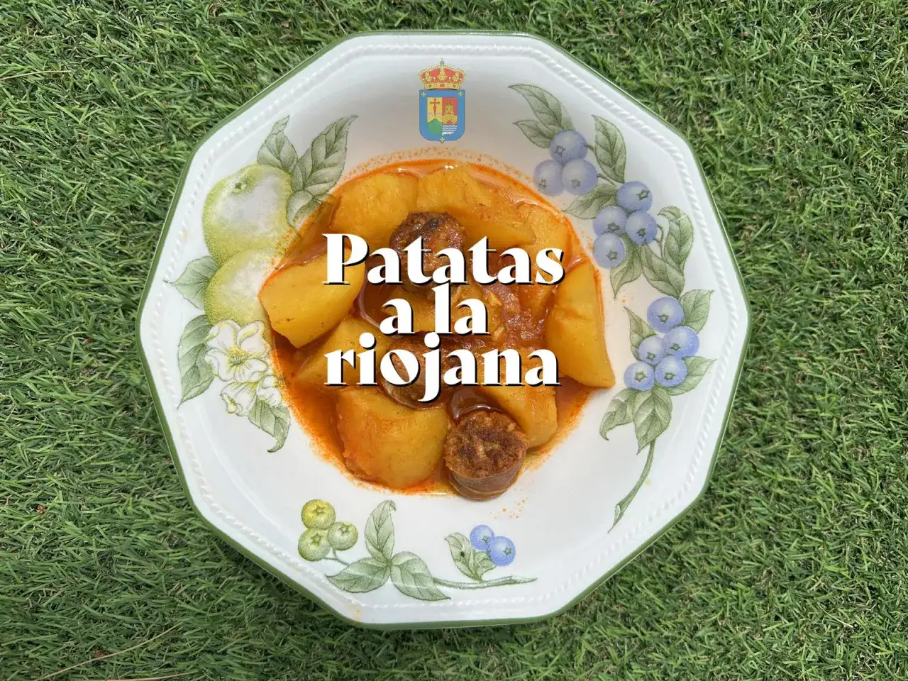 Un plato de patatas a la riojana, con trozos de chorizo y patata en una salsa rojiza, servido en una vajilla decorada con frutas y bayas.