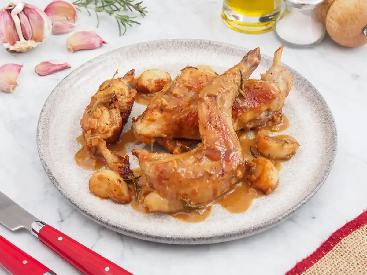Delicioso conejo al ajillo servido en un plato, con trozos de ajo asado y romero.