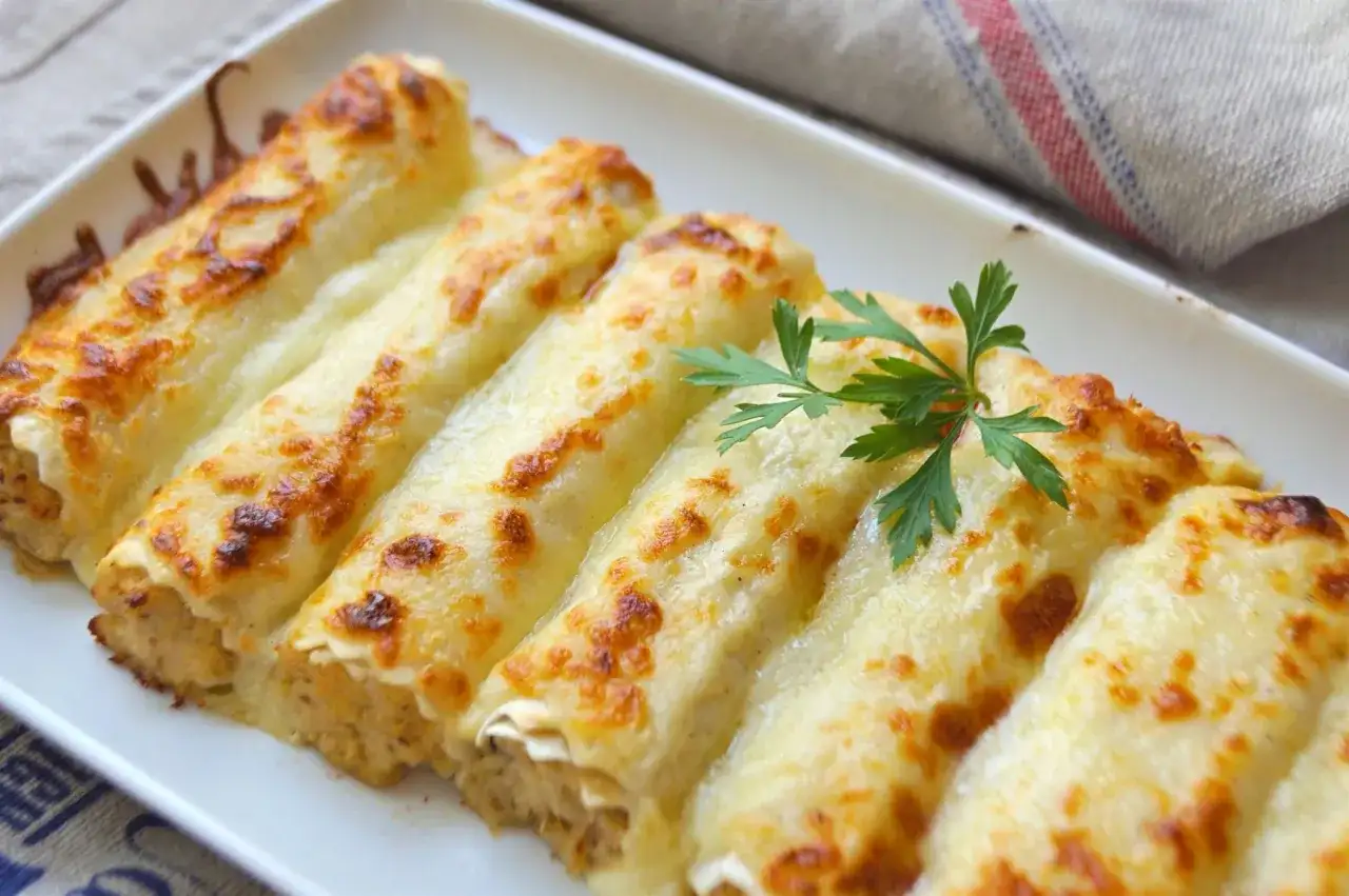 Canelones de pollo gratinados, cubiertos con queso derretido y dorados, decorados con perejil fresco.