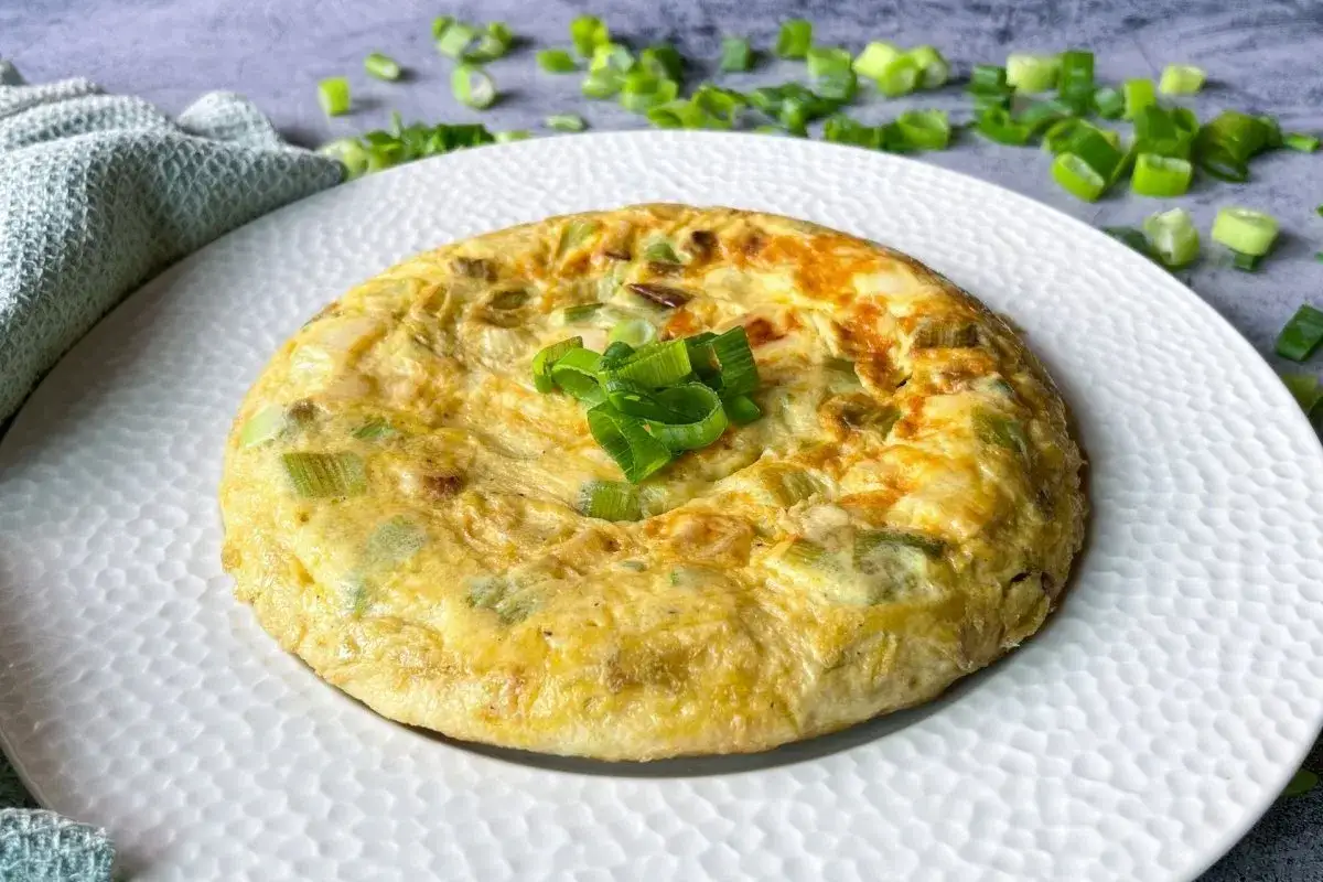 Tortilla de ajetes dorada y esponjosa, decorada con cebolleta fresca picada. Un plato sencillo y delicioso.
